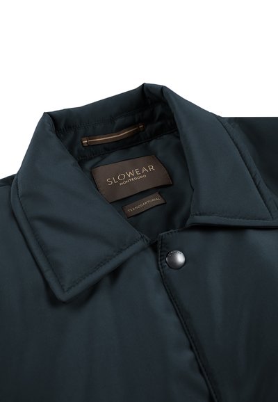 Giacca color verde scuro con colletto e texture liscia. Presenta un bottone a pressione e un'etichetta con la scritta "Slowear Montedoro" in lettere dorate.