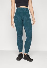 Hoge taille teal leggings met een subtiele camouflageprint, gemaakt van rekbaar materiaal, gecombineerd met zwarte sportschoenen.