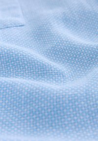 Hele sinist värvi tekstuuriga kangas, millel on kujundatud mustriga väikesed valged ruudud. Pehme ja sile pind, sobib riietuseks või kodutekstiilideks.