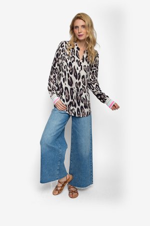 Blouse met lange mouwen in luipaardprint en een V-hals, gecombineerd met wijde blauwe spijkerbroeken en bruine sandalen met bandjes en een platte zool.