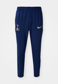 Marineblå træningsbukser med elastisk talje, der har et gult Nike-logo og et broderet klubmærke på venstre lår. Glat stof.