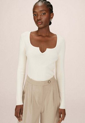 Haut blanc à manches longues côtelé avec un large col en scoop, associé à un pantalon beige taille haute doté d'un détail de bouton.