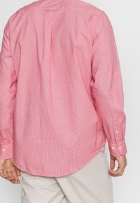 Lichtroze katoenen shirt met lange mouwen, voorzien van een subtiel textuurpatroon, afgeronde zoom en knoopsluitingen aan de manchetten. Achterpand met jukdetail.