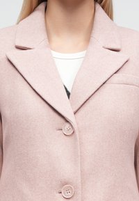 Casaco rosa em mistura de lã com lapelas entalhadas, dois botões e um bolso ao peito. Textura suave, design ajustado e detalhes simples.