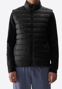 Schwarze gepolsterte Weste mit hohem Kragen und durchgehendem Reißverschluss, mit glatter Textur und integrierten Taschen, die über einem langen schwarzen Oberteil getragen wird.