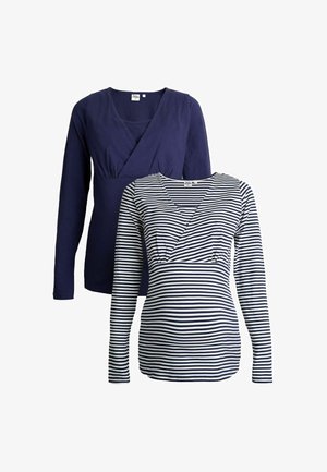 Divas divu garo piedurkņu krekli: viens ir viendabīgs tumši zils ar V-veida kaklu un savilkšanu krūšu rajonā, bet otrs ir balts un tumši zilā svītrā ar krustojuma dizainu.