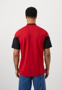 Κόκκινο και μαύρο κοντομάνικο πόλο μπλουζάκι με στέρεο σώμα, αντίθετους μανίκους και κλασικό γιακά. Διαθέτει λεία υφή.