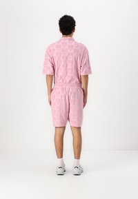 Pink short-sleeve shirt and shorts set with embossed pattern. Elastic waistband. Lightweight fabric, worn with white socks and sneakers.