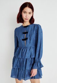 Vestido azul plissado com três laços pretos, mangas longas e um design em camadas com uma abertura em forma de chave na gola.