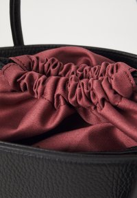 Black leather handbag featuring a gathered maroon lining. The interior showcases a smooth texture with a drawstring closure design.