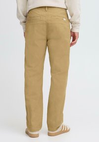 Khaki pants made of cotton blend, straight leg design, two back pockets, and subtle branding near the waistband. Paired with white sneakers.
