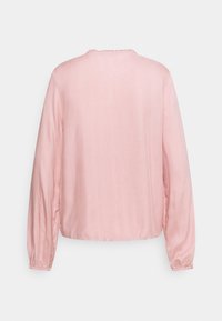Blusa a maniche lunghe rosa chiaro con scollo rotondo e polsini arricciati, realizzata in un tessuto morbido e leggero.