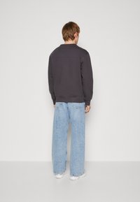 Donkergrijze sweatshirt, ontspannen pasvorm met een geribbeld zoom, gecombineerd met lichtblauwe wijde jeans en witte sneakers. Eenvoudig ontwerp, gladde textuur.