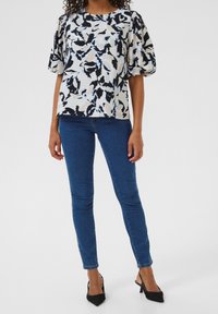 Geprinte blouse met ballonmouwen in roomkleur, blauw en zwart; gecombineerd met blauwe skinny jeans en zwarte puntige hakken.