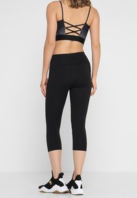 Černá sportovní podprsenka s křížovými ramínky na zadní straně, spárovaná s černými krátkými legínami a černými teniskami s bílými akcenty.