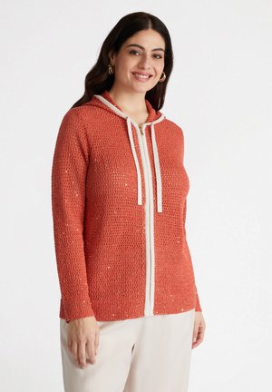 Sweat à capuche zippé en tricot corail avec un motif texturé, cordons de serrage crème et poignets côtelés. Comprend une fermeture éclair sur le devant et une capuche.