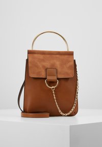 Ruskea nahkakäsilaukku, jossa on karhea mokkanahkakansi, pyöreä kultahaave ja ketjunkantohihna. Etuosassa on rengaskoriste.