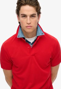 Polo rosso con colletto a bottoni, colletto di jeans sovrapposto, maniche corte e texture a costine.