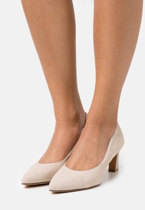 Chaussures à talons en daim beige avec un bout pointu et un talon bloc modéré. Texture lisse, design minimaliste et sans motifs ni accents visibles.