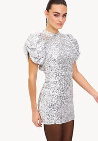Zilveren pailletten mini-jurk met pofmouwen, hoge halslijn en aansluitende silhouet. Glad textuur met reflecterend oppervlak en korte lengte.