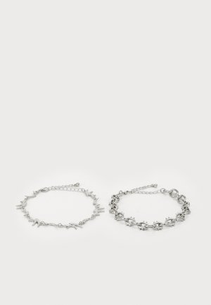 Two silver bracelets displayed side by side. One features a delicate chain with bird-shaped accents; the other has a bold, spiked design.