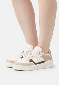 Zapatilla elegante con una combinación de cuero beige y rosa claro, acentos en verde oliva, panel lateral texturizado y una suela blanca gruesa.