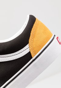 Black canvas shoe with a yellow suede heel accent, white stripe detail, and a textured white rubber sole.