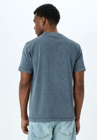 Kortärmad grå t-shirt med en blekt, texturerad yta; har en rund halsringning och synlig sömnad, tillsammans med ljusblå denimshorts.