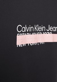 T-shirt in cotone nero con testo bianco "Calvin Klein Jeans ESTABLISHED 1978" e una sovrapposizione a strisce testurizzate rosa con "NEW YORK, NY."