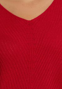 Czerwony sweter dzianinowy z dekoltem w serek, teksturowanym ściągaczem i subtelnymi detalami ściegów. Lekki i przewiewny materiał, dopasowany krój.