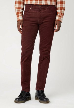 Pantalon en velours côtelé bordeaux à coupe slim, comportant cinq poches, fermeture à bouton et texture subtile. Assorti à des bottes noires à lacets.