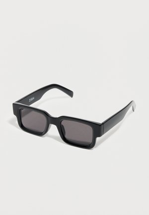Black rectangular sunglasses with thick frames and dark lenses, resting on a white surface.
