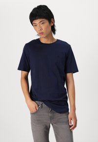 Marineblaue Kurzarm-T-Shirt aus Baumwollstoff mit rundem Halsausschnitt. Mit einem kleinen, schwarzen Logo auf der Brust und einem lässigen Schnitt.