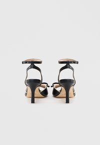 Czarne sandały na wysokim obcasie z eleganckim wzornictwem, otwartym tyłem, cienkim paskiem wokół kostki oraz teksturowaną podeszwą, na smukłym obcasie typu szpilka.