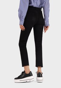 Jeans neri a vita medio-alta con taglio dritto e orlo sfrangiato. Abbinati a sneakers nere con piattaforma e suola e lacci bianchi. Camicia a righe blu.