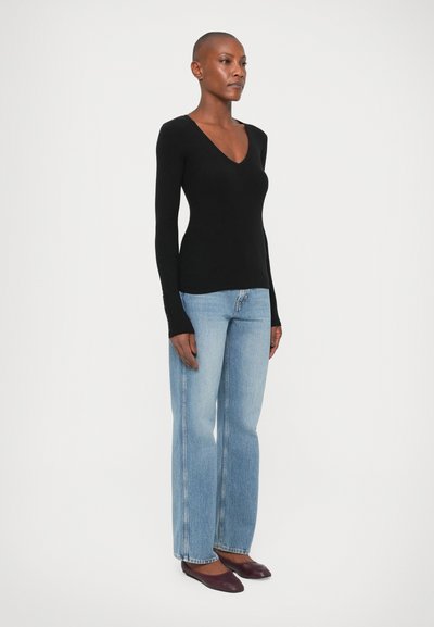 Tricou negru cu maneci lungi și decolteu în V, realizat dintr-un material elastic, asociat cu blugi ușor evazați de culoare albastru deschis. Încălțămintea este o pereche de balerini violet închis.