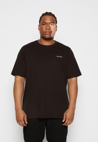 Sort bomulds t-shirt med korte ærmer, der har et lille hvidt Calvin Klein-logo på venstre brystområde. Enkel, lige skåret design.