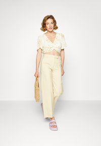 Top cropped floral claro, calças largas bege, sandálias lavanda e uma bolsa de vime. Apresenta cores suaves e um corte descontraído, com uma superfície texturizada.