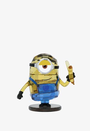 Una figura de Minion colorida y cristalina sostiene un plátano, vistiendo un overol azul y guantes negros, sobre un fondo blanco.