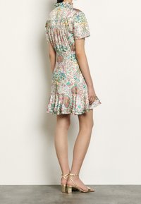 Blumenmusterkleid mit kurzen Ärmeln, aufgerüschtem Saum und taillierter Taille. Merkmale sind Pastellfarben, ein hoher Ausschnitt und fließender Stoff. Goldene Absatzsandalen.