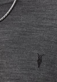 Grauer Strickpullover mit gerippter Textur und kleinem, schwarzen, gesticktem Logo auf der Brust. Leichtgewichtig mit Rundhalsausschnitt.