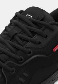 Pantofii sport negri au un superior sintetic texturat, șireturi plate și accente de marcă. Dispun de un guler căptușit și o talpă din cauciuc pentru aderență.