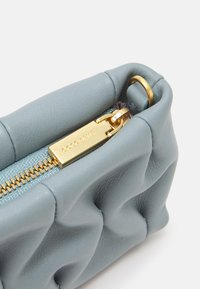 Bolsito de cuero azul claro con un diseño acolchado, hardware de cremallera dorada y una etiqueta de la marca. Presenta una textura suave y bordes redondeados.