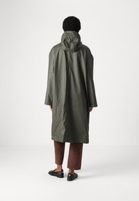 Vannbestandig olivengrønn kåpe med hette, lange ermer og rett snitt. Jevn tekstur, minimal hardvare og udetaljert design.