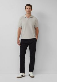 Polo shirt gris clair texturé à manches courtes, associé à un pantalon noir et des baskets blanches avec un accent marron.