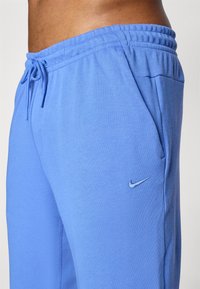 Kék melegítőnadrág, puha anyagból készült, rugalmas derékkal és zsinórral, valamint egy kis hímzett Nike logóval kék színben.