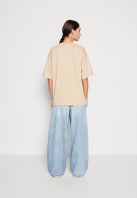 Beige oversized skjorte med korte ærmer, parret med lyseblå brede jeans. Glat stof med en afslappet pasform og enkelt design.