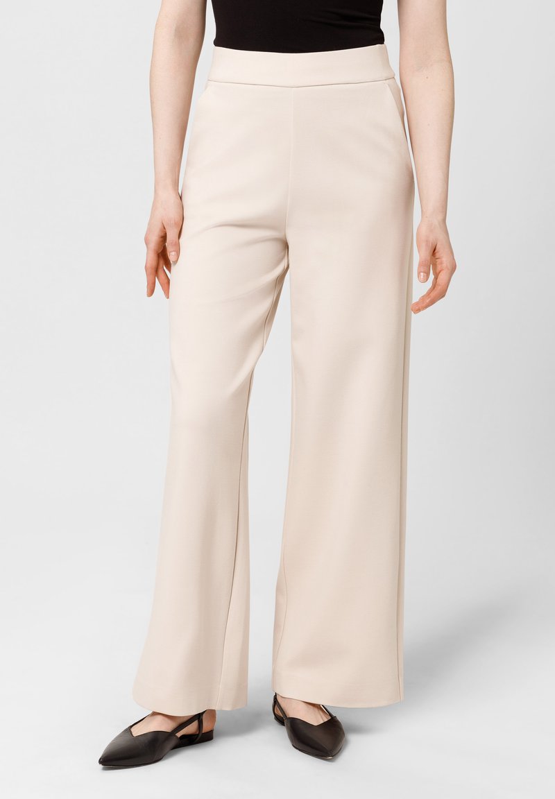 Beige wijde-pijpen broeken met een zachte textuur, hoge tailleband en subtiele zijnaaddetails, gecombineerd met donkere puntige flats.