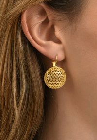 Boucles d'oreilles circulaires en ton or avec un design en treillis complexe, suspendues à un simple crochet en métal. Surface texturée et finition réfléchissante.