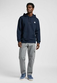 Sudadera navy con bolsillo tipo canguro en el frente, capucha con cordón, combinada con pantalones cargo gris claro con bolsillos laterales y pernera ajustada. Zapatillas azules.